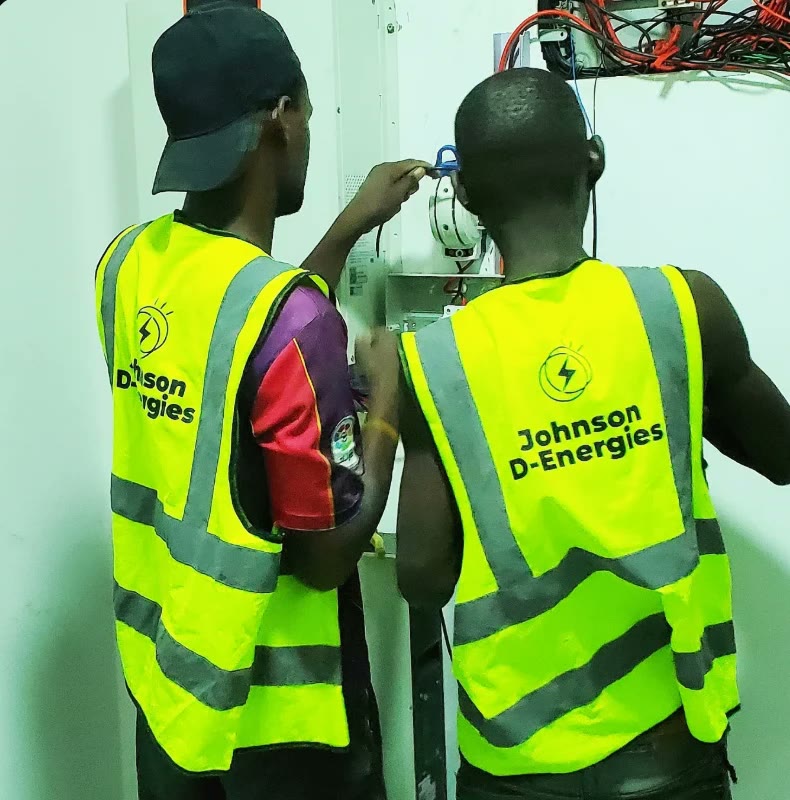 Two technicians in Johnson D-Energies vests wiring a breaker panel